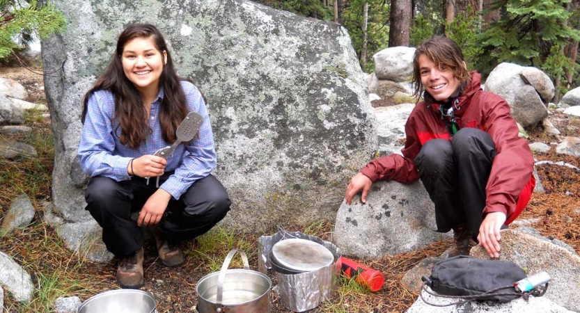 two young people use camping stoves to prepare food on on outward bound course